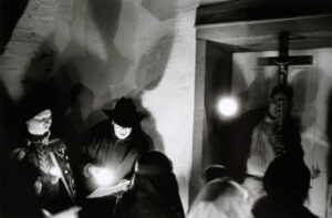 A man in a hat and a black jacket is holding a guitar