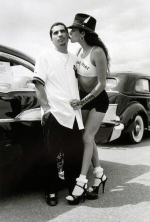 A man and woman kissing in front of old cars.