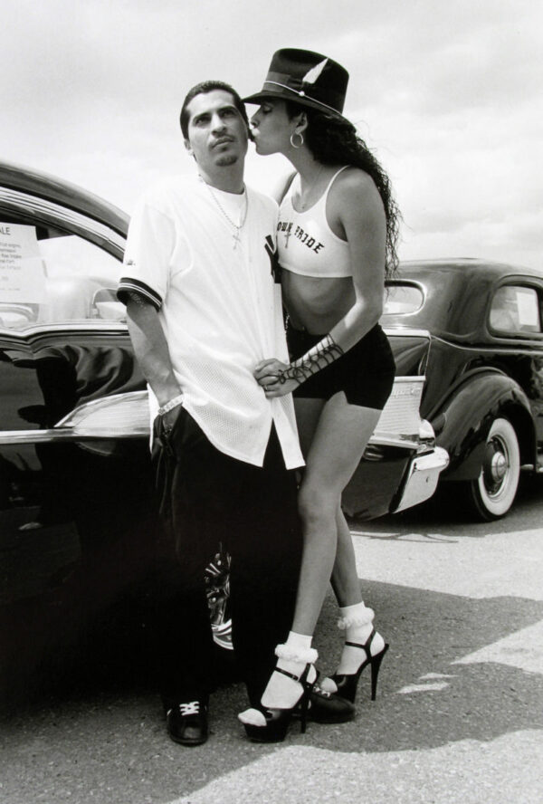 A man and woman kissing in front of old cars.