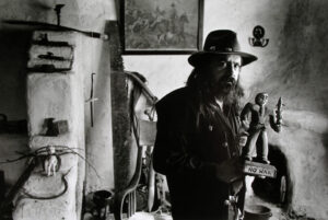 A man in a hat and jacket standing next to a wall.