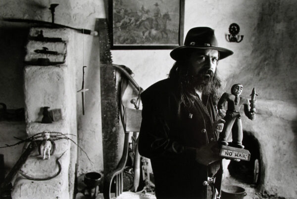 A man in a hat and jacket standing next to a wall.