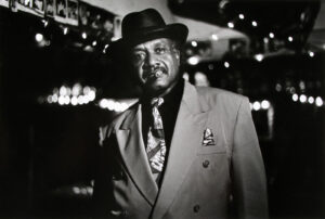 A man in a suit and hat standing outside.