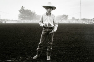 A young cowboy stands in the middle of an open field.
