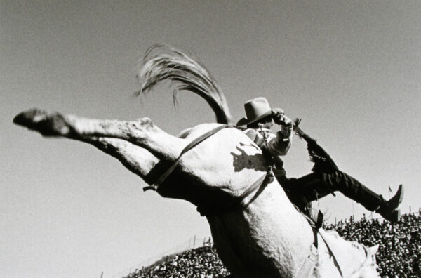 A man on horseback is jumping over another horse.