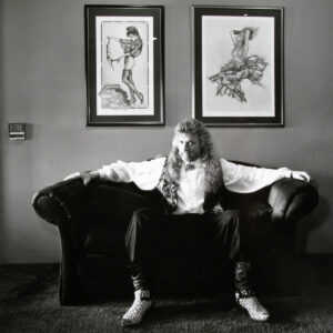 A man sitting on top of a couch in front of two framed pictures.