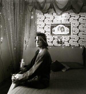 A woman sitting on the bed in front of a wall with pictures.