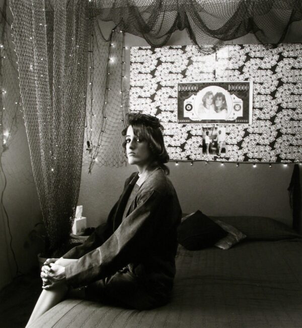 A woman sitting on the bed in front of a wall with pictures.