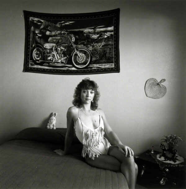 A woman sitting on the bed under a motorcycle banner.