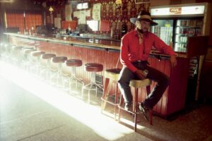 A man sitting on top of a stool in front of a bar.