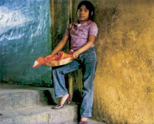 A young girl holding an umbrella in front of a wall.