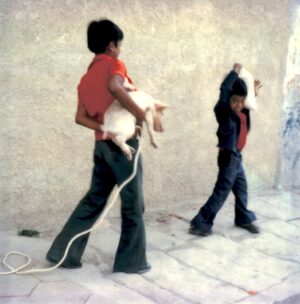 Two young boys are walking on the sidewalk.
