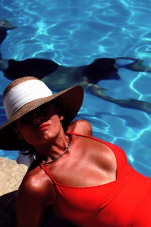 A woman in a hat and red bikini sitting on the edge of a pool.