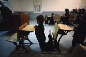 A child is sitting in front of two desks.