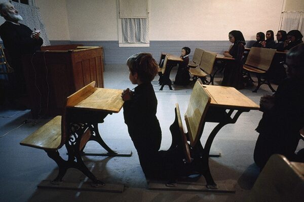 A child is sitting in front of two desks.