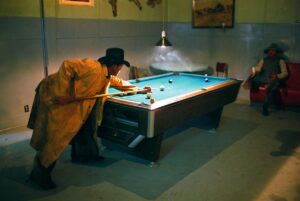 A man in yellow jacket playing pool on a table.
