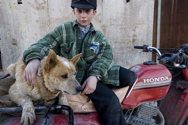 A boy sitting on the back of a red motorcycle with his dog.