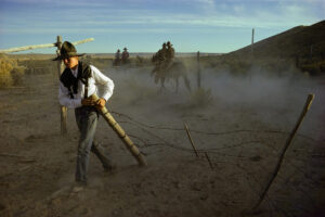 A man in white shirt and hat holding a stick.