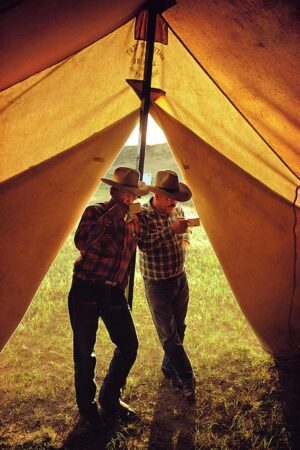 Two men in cowboy hats standing inside a tent.