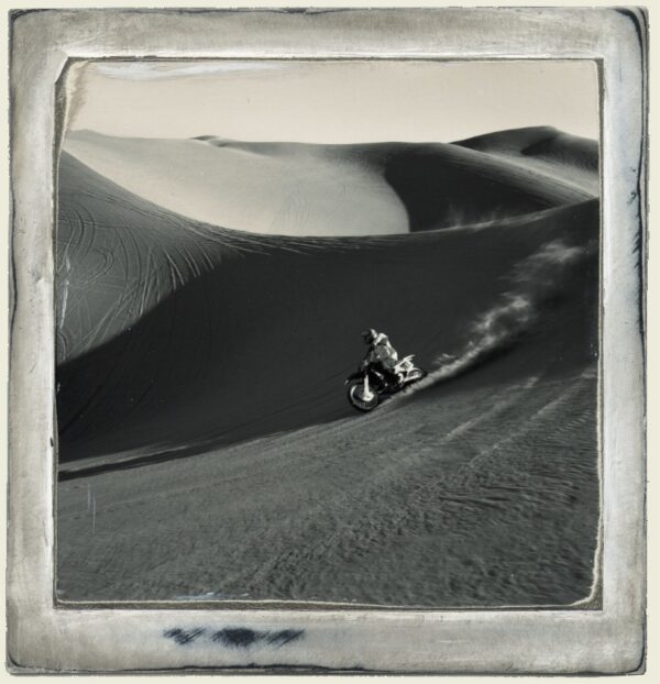 A person riding a motorcycle on top of a sand dune.