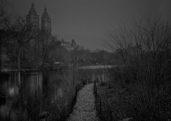 A black and white photo of a lake with trees in the background.