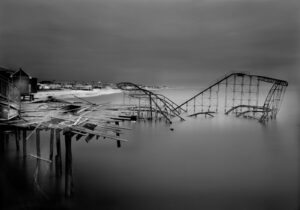A roller coaster is in the water near some piers.