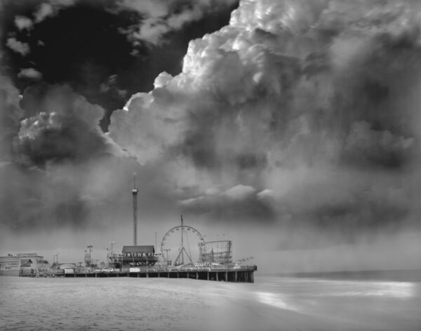 A black and white photo of the ocean with a ferris wheel in it.