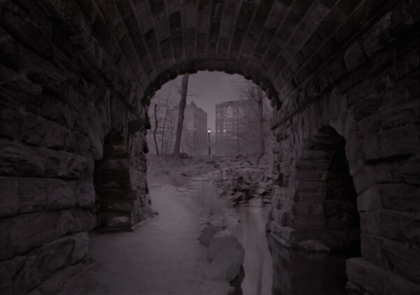 A dark picture of an old tunnel with a person walking through it.