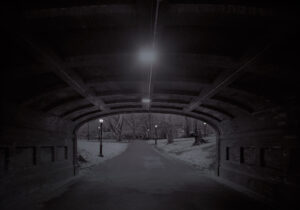 A dark tunnel with lights and trees in the background.