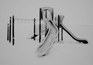 A black and white photo of a playground in the snow.