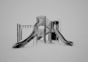 A black and white photo of a playground in the snow.