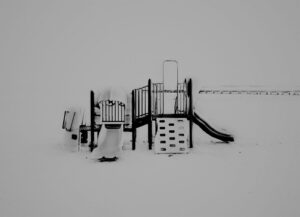 A playground in the snow with slides and swings.