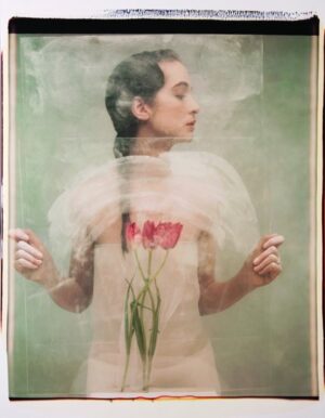 A woman holding flowers in her arms and standing behind a painting.