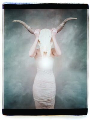 A woman in white dress holding her head with horns.
