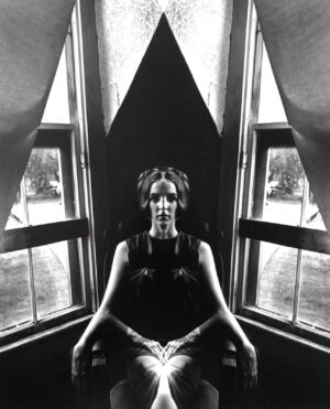 A woman sitting in front of two windows.