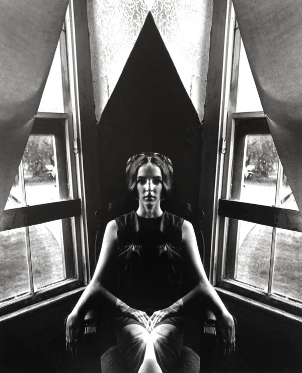 A woman sitting in front of two windows.