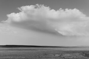 A black and white photo of a field with clouds in the background.