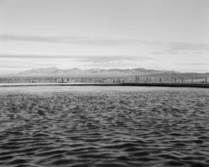 A black and white photo of the ocean with mountains in the background.