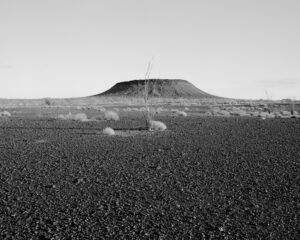 A black and white photo of a field with a hill in the background.