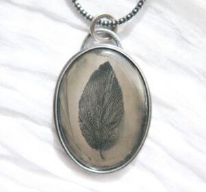 A leaf in a glass is shown on a necklace.