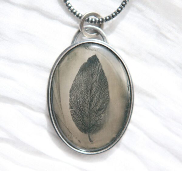 A leaf in a glass is shown on a necklace.