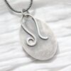 A silver necklace with an oval shaped pendant.