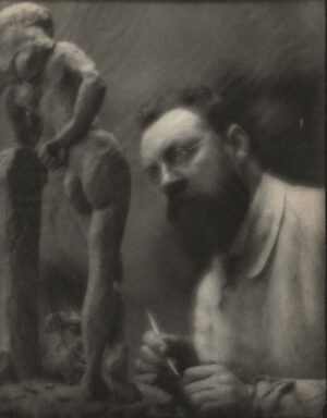 A man with a beard and mustache is in front of a statue.