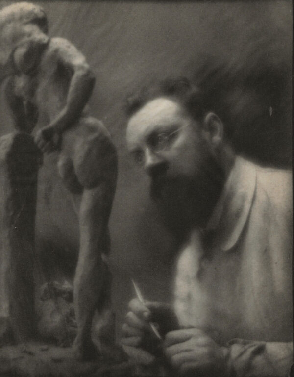 A man with a beard and mustache is in front of a statue.