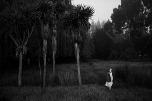 A woman in white dress standing next to trees.