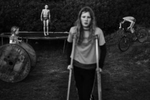 A woman with crutches stands in front of a boy.