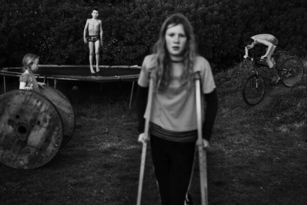 A woman with crutches stands in front of a boy.