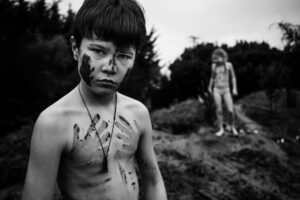 A young boy with face paint and necklace standing in front of another man.