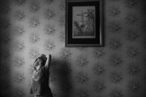 A child standing in front of a wall with a picture hanging on it.