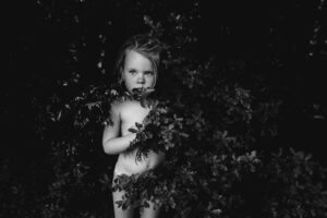A naked child standing in the bushes