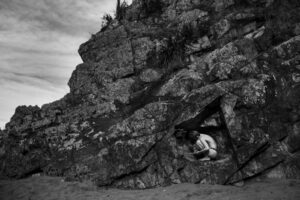 A person sitting on the ground in front of a rock.